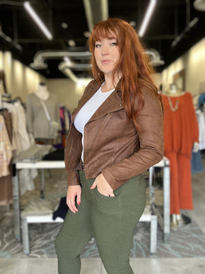 Woman wearing a brown leather jacket and green pants in a clothing store.