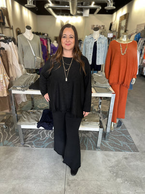 Woman in a black outfit standing in a clothing store with racks of clothes in the background.