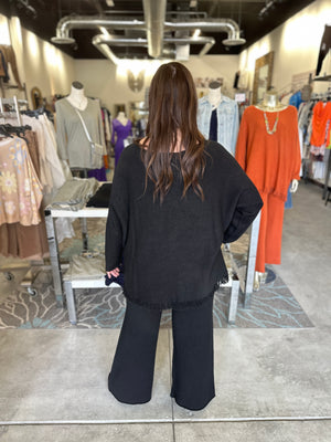 Woman in a black outfit standing in a clothing store with racks of clothes around her.