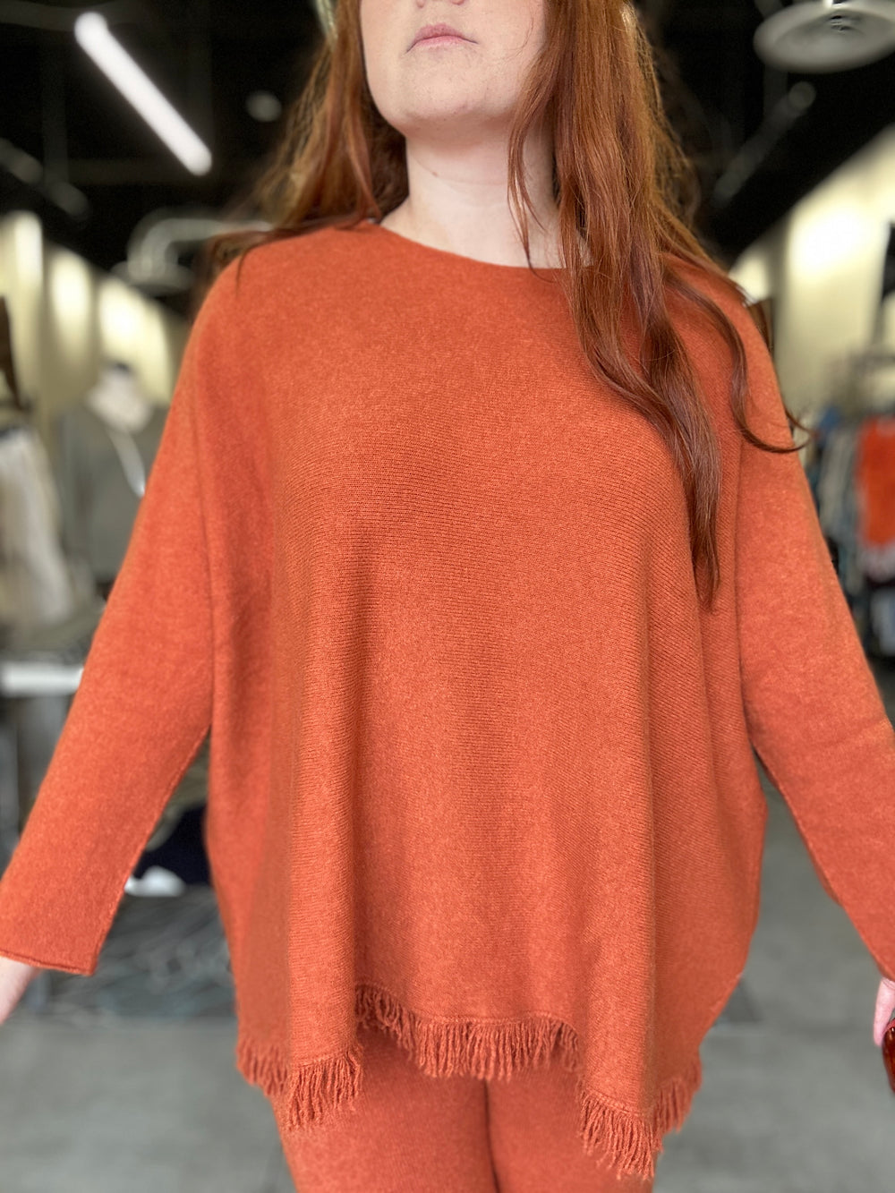 Person wearing a rust-colored poncho with fringe details indoors.